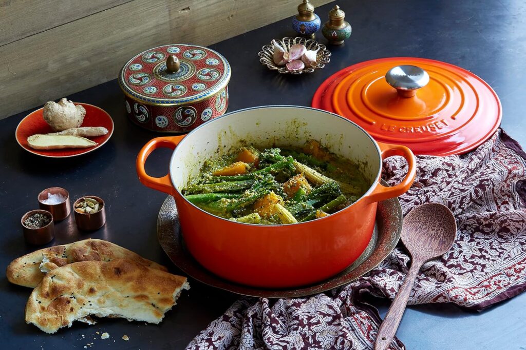 Red cast iron Dutch oven with a lid, containing beef stew with vegetables, on a gray trivet, on a wooden table.
